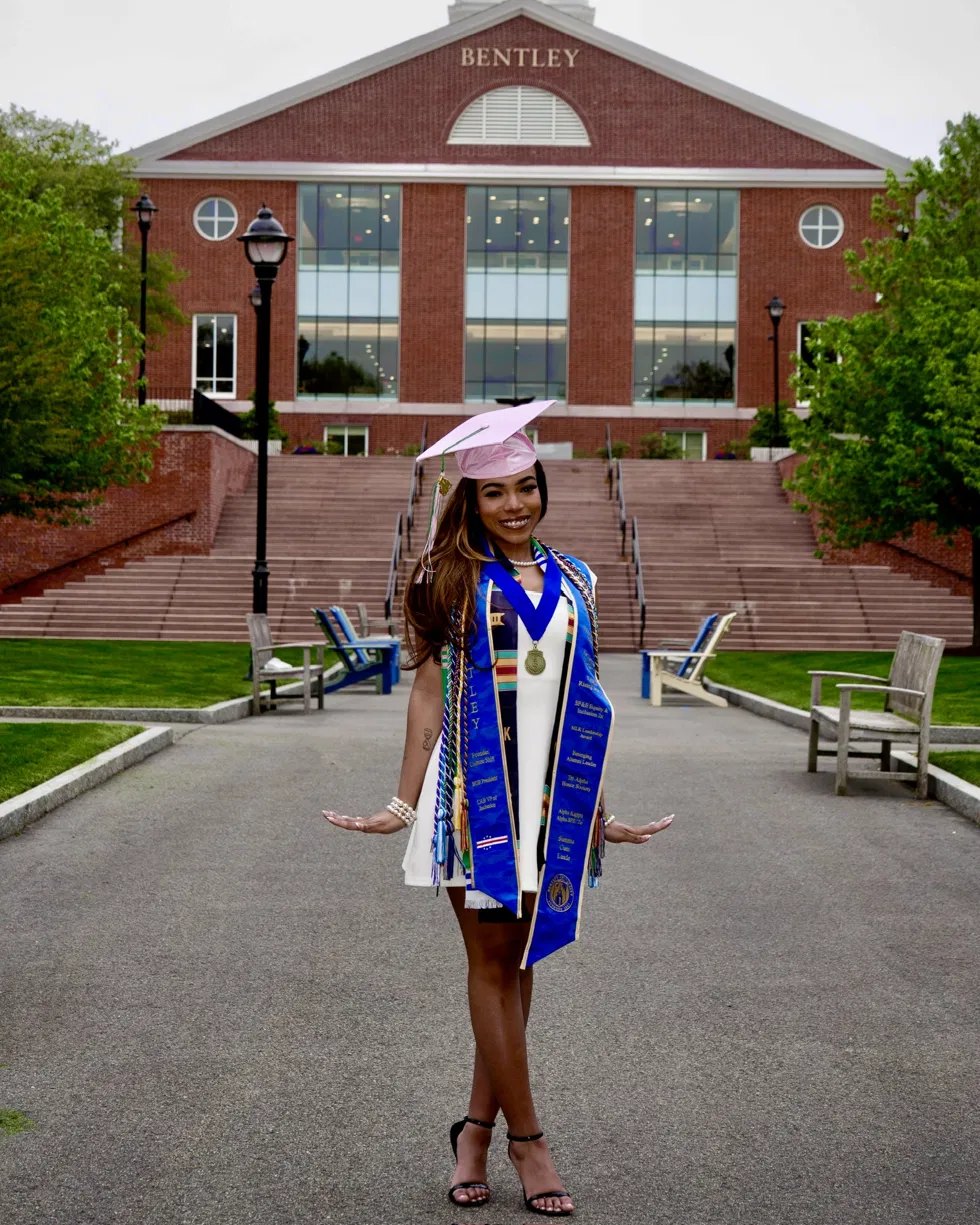 Jaychele in her graduation cap, honors stoles and cords in front of Bentley University.